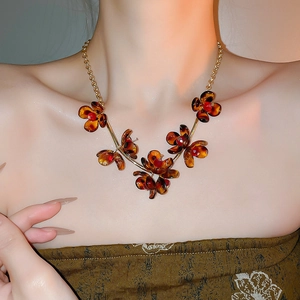 Detail of amber flower necklace with red accents on a gold chain worn by a model