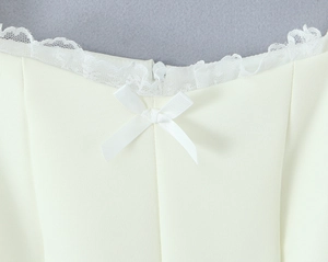 Detail der Spitzenborte am Ausschnitt mit einer Satinschleife an einem cremefarbenen Kleid