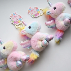Detail of three iridescent unicorn plush keychains with sparkly wings and gold metal rings