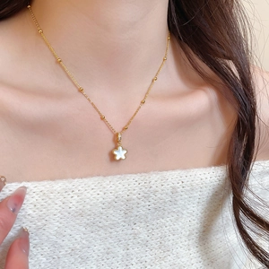 Close-up of golden beaded chain with white five-petal flower pendant on female neck
