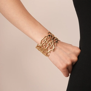 Macro detail of golden branch-textured open cuff bracelet with coral design on wrist