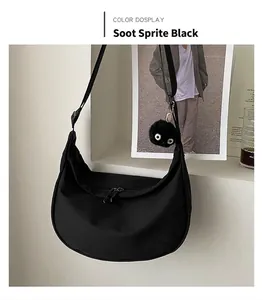 Close-up of black nylon crescent bag with adjustable strap and plush soot sprite charm