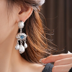 Macro shot of French vintage pearl earrings featuring a blue evil eye and silver tassels