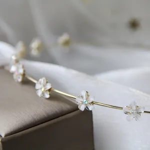Dettaglio del cerchietto in metallo dorato con fiori bianchi e centri in strass lucidi