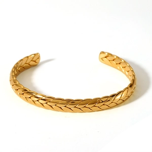 Close-up of golden stainless steel open cuff bracelet with woven wheat texture detailing