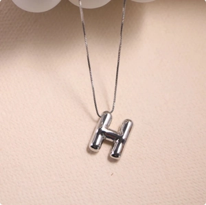 Macro shot of a 3D silver letter H pendant with a high-polished finish on a fine chain