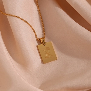 Macro shot of 18K gold rectangle pendant with sun gesture on pink silk fabric