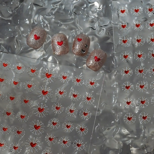 Detail of red heart nail stickers with gold rays on glittery pink press-on nails