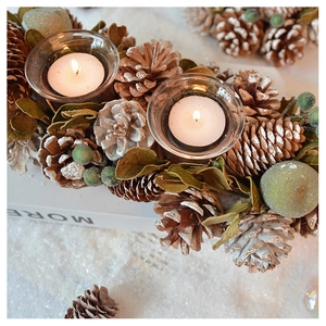 Detail of pine cones, red berries and glass candle holders on a snowy background