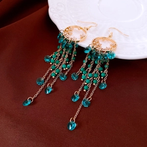 Detail of ethnic tassel earrings with gold moons, green beads and blue crystals