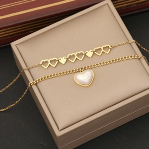 Double-layered golden stainless steel heart and pearl necklace on a beige jewelry box