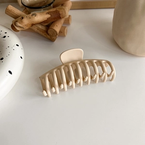 Close-up of a large beige matte hair claw clip on a warm aesthetic wooden background