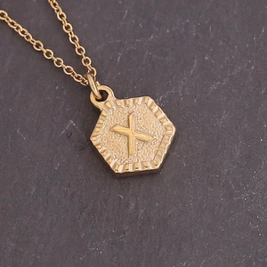 Detailed macro view of a gold hexagonal pendant featuring the embossed letter X on a chain