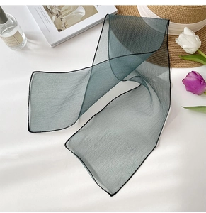 Macro detail of sheer dark green organza scarf with fine black edge stitching and texture