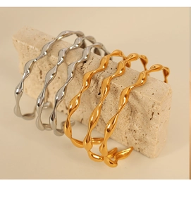Detail of geometric wave-shaped gold and silver bangles on a textured stone base