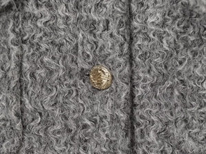 Détail macro du bouton martelé doré sur la texture de laine bouclée grise