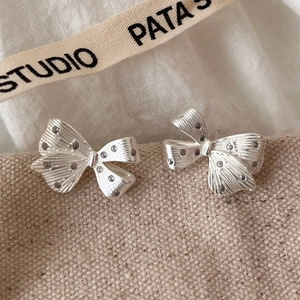 Silver bow stud earrings with sparkling crystals on minimalist textured metal surface