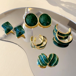 Macro shot of geometric emerald green enamel and gold plated earrings on a mirror