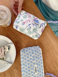 Floral canvas makeup bag with zipper and purple strap on a wooden table with coffee