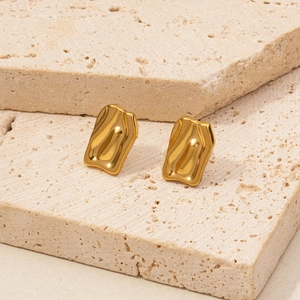 Macro view of gold bow-shaped lava wave earrings on a textured stone surface