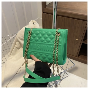 Detail of green quilted handbag featuring a gold chain strap and embossed Fashion text