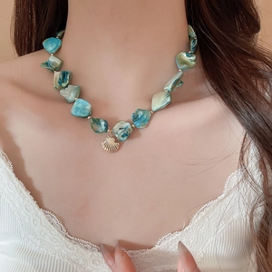 Detail of blue shell necklace on model showing irregular marble beads and gold pendant