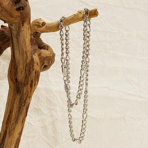 Gros plan d'un collier Figaro en acier inoxydable argenté sur une branche en bois rustique