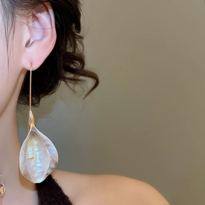 Détail d'une boucle d'oreille dorée avec un pendentif pétale blanc nacré porté par un mannequin
