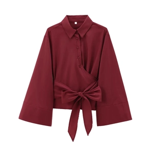 Détail d'une chemise bordeaux à manches longues avec nœud à la taille et boutons dorés