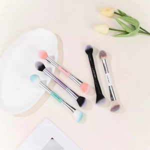 Double-headed makeup brushes in five colors with gradient bristles on a beige table