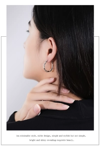 Macro detail of silver S925 irregular wave hoop earring on female model ear