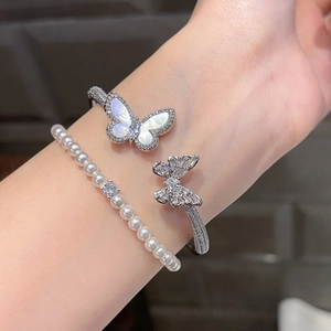 Detail of silver butterfly cuff with shell wings and pearl bracelet featuring square zircon