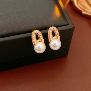Détail de boucles d'oreilles dorées en U avec zircons et élégante perle blanche pendante