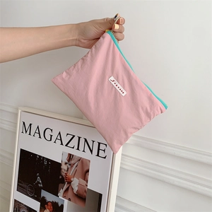 Pink nylon cosmetic pouch with blue zipper and logo label held against magazine