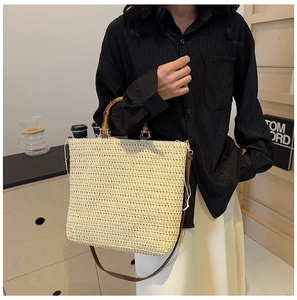 Detail of beige straw bag with bamboo handles and removable brown leather strap