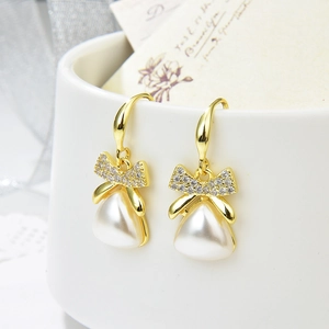 Elegant gold bow earrings with baroque pearls and zircons hanging on a ceramic vase