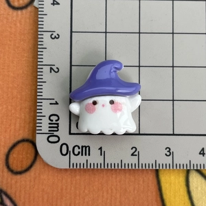 Detail view of mini white resin ghost charm with purple wizard hat on a ruler