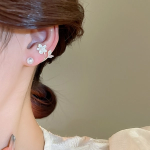 Detail of floral earring with white pearl and zircon leaves on a golden base