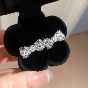 Dettaglio macro del fermaglio a fiocco argento con zirconi luccicanti e doppie perle bianche