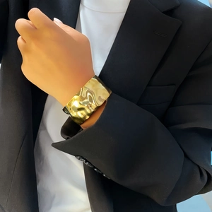 Detail of wide gold irregular hammered cuff bracelet worn by model with black blazer