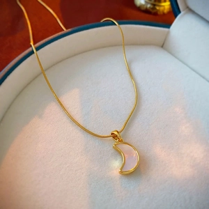 Detail of a crescent moon pendant necklace with white inlay and golden snake chain