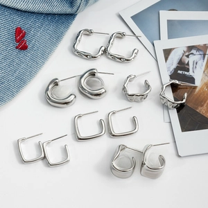 Collection of geometric square and C-shaped stainless steel earrings on denim backdrop