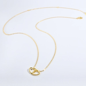 Close-up of interlocking heart pendants in gold finish with smooth and beaded textures
