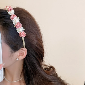 Detail of pink and beige satin fabric flowers on a gold metal headband worn by model