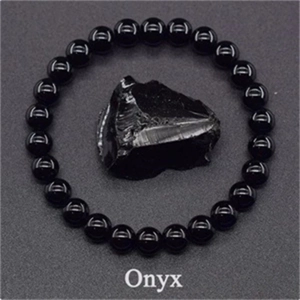 Macro shot of an 8mm black onyx beaded bracelet encircling a natural raw onyx stone