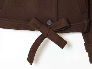 Detail view of dark brown wool jacket hem with black button and waist tie strap texture