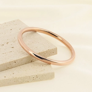 Detail view of a 6mm rose gold stainless steel bangle on a beige travertine stone surface