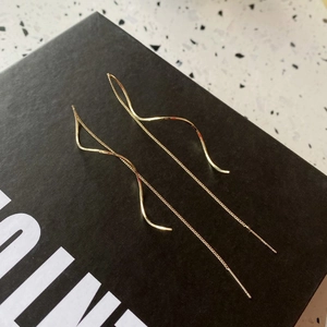 Modern gold wave pull-through earrings displayed on a premium black gift box