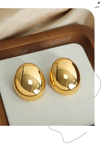 Macro shot of gold oval egg-shaped stud earrings with high mirror polish on wooden tray