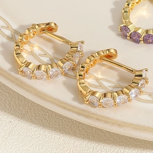 Détail de boucles d'oreilles créoles dorées avec zircons violets et blancs étincelants